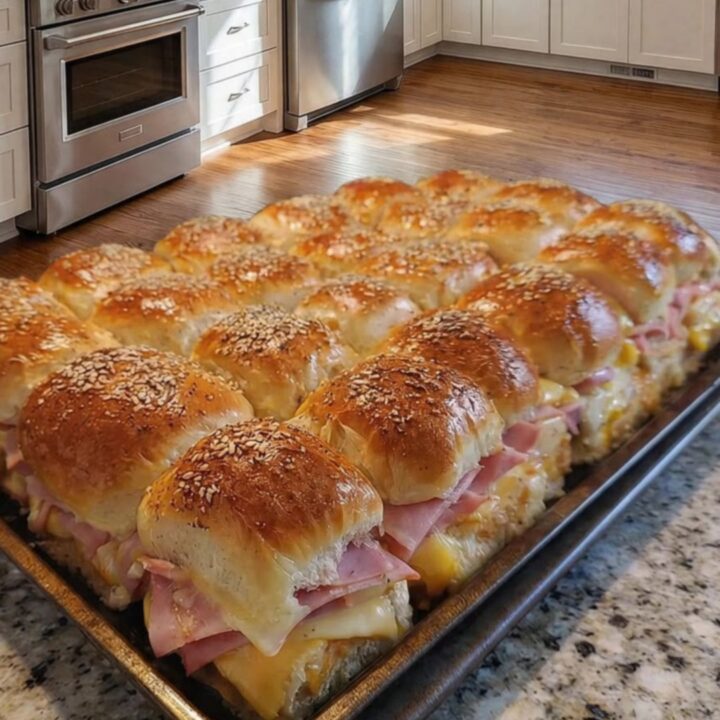 Mini-sandwichs au jambon et fromage dorés et brillants sur une plaque de cuisson.