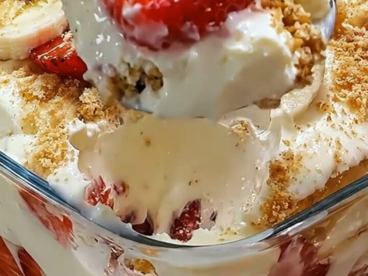 A close-up of a glass filled with layers of vanilla pudding, sliced strawberries, bananas, and a golden cookie crumb topping.