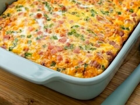 A golden-brown farmer's breakfast casserole with bubbling cheese, ham, and green onions in a blue baking dish.
