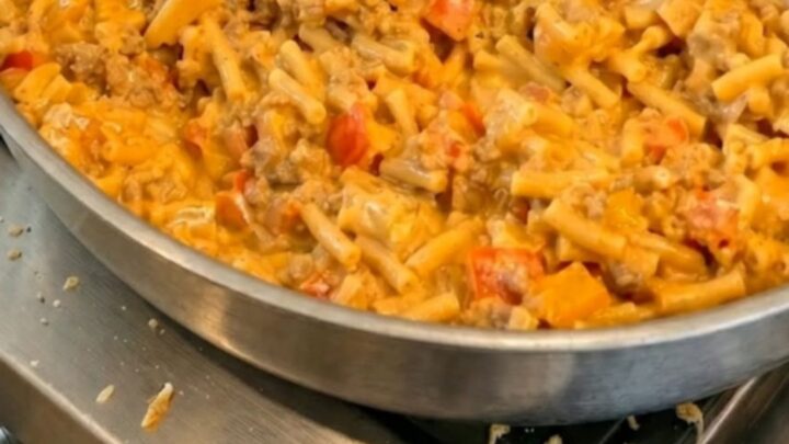 A serving spoon scooping creamy taco macaroni and cheese from a skillet with a long stretch of melted cheese.
