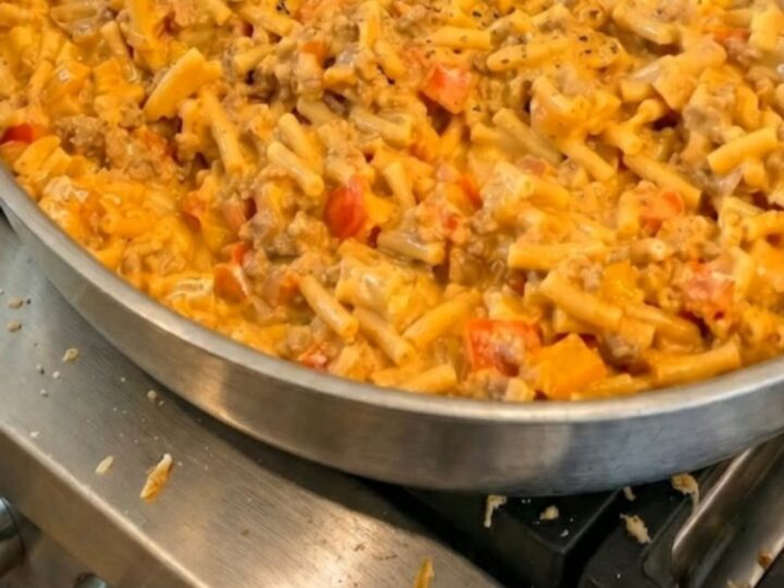 A serving spoon scooping creamy taco macaroni and cheese from a skillet with a long stretch of melted cheese.