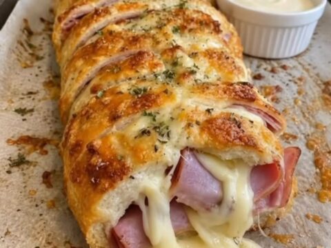 Une miche de pain dorée et farcie au fromage fondant, posée sur du papier cuisson.