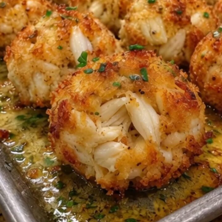 Two fingers breaking open a golden, crispy crab bomb to reveal steaming, tender jumbo lump crab meat inside.
