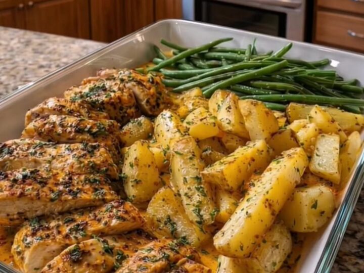 A rustic baking dish filled with golden roasted chicken breast, crispy potato wedges, and green beans.