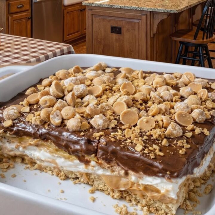 A close-up of a square piece of peanut butter crunch lasagna showing distinct layers in a white dish.