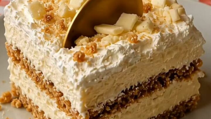 A square slice of no-bake white chocolate biscuit cake on a white plate with a golden spoon.