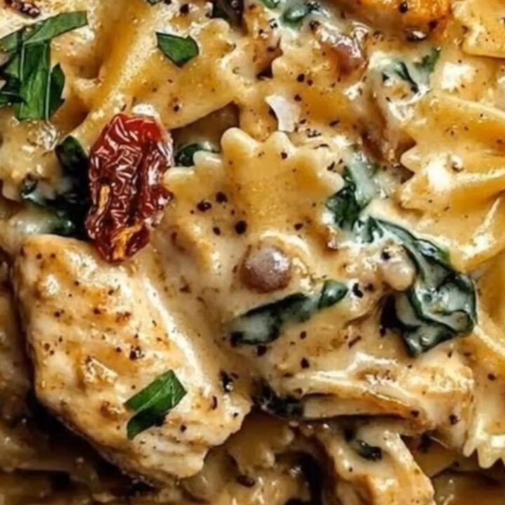 A fork lifting rich, creamy farfalle pasta and juicy seared chicken dripping with velvety sauce and sun-dried tomatoes.