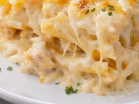 A square portion of creamy Chicken Alfredo Bake on a white plate, topped with golden melted cheese and fresh parsley.