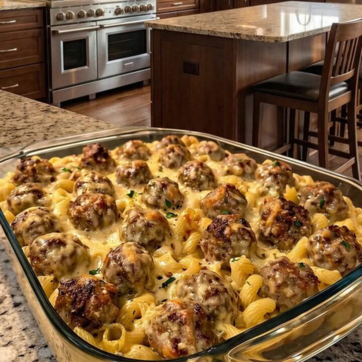 A close-up of a creamy Swedish meatball noodle bake in a clear dish with golden melted cheese.