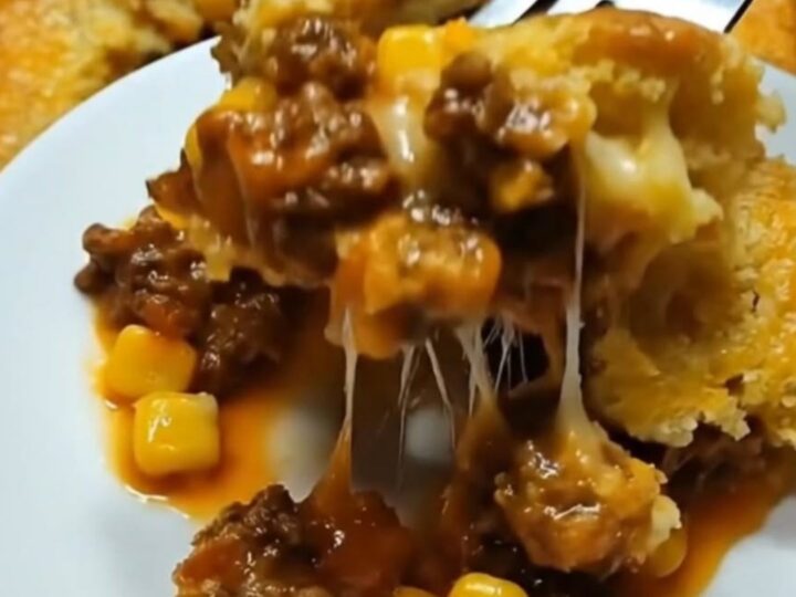 A steaming slice of cowboy cornbread casserole on a white plate showing layers of savory beef, corn, melted cheese
