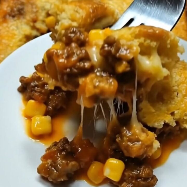 A steaming slice of cowboy cornbread casserole on a white plate showing layers of savory beef, corn, melted cheese
