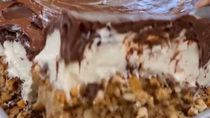 A thick, decadent slice of chilled chocolate eclair cake lifted from a metal pan, showing creamy layers.