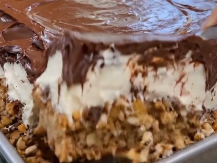 A thick, decadent slice of chilled chocolate eclair cake lifted from a metal pan, showing creamy layers.