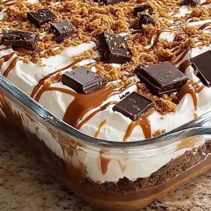 A glass dish filled with layers of dark chocolate, whipped cream, and caramel, topped with cookie crumbles.