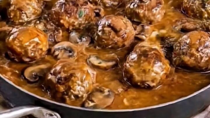 A large black skillet filled with golden-brown beef meatballs covered in a creamy mushroom sauce and garnished with parsley.