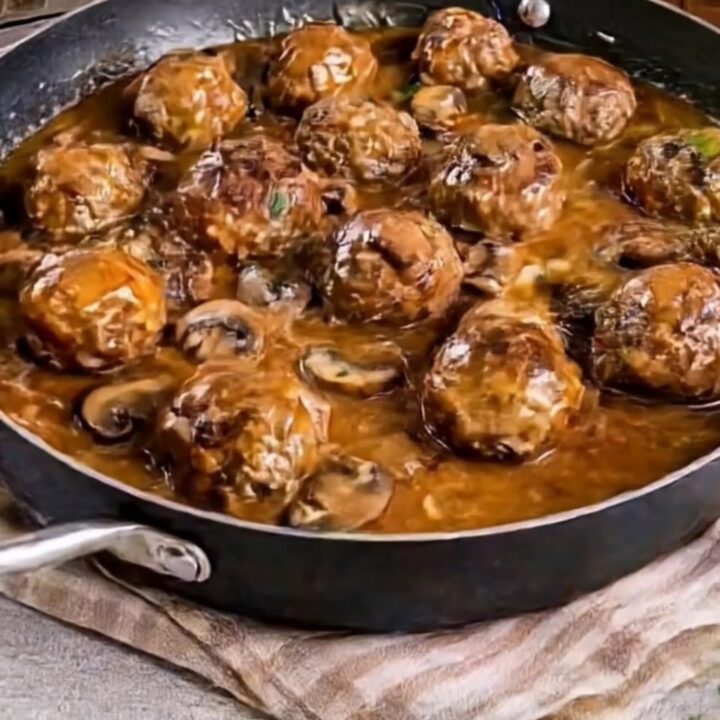 A large black skillet filled with golden-brown beef meatballs covered in a creamy mushroom sauce and garnished with parsley.
