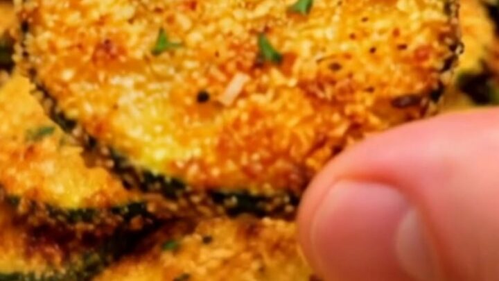 A pile of golden, crispy parmesan zucchini chips dusted with fresh thyme leaves on a white plate.