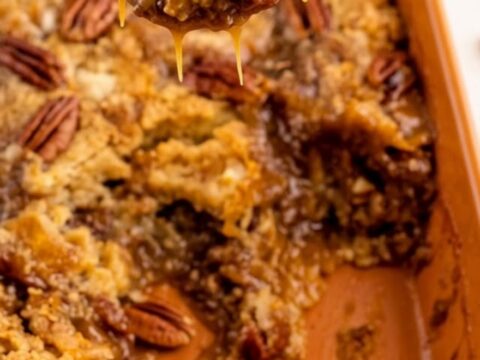 A warm, gooey scoop of sugar-free pecan pie dump cake being lifted with a silver spoon from an orange baking dish