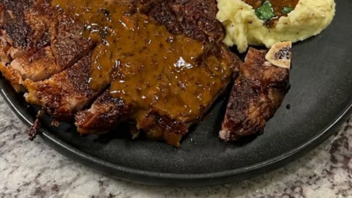 A plate featuring sliced seared steak, creamy mashed potatoes, and herb gravy on a granite surface.
