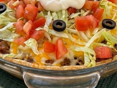 A hearty slice of cheesy taco pie being lifted from a glass dish, showing a golden crust and melted cheddar stretch.