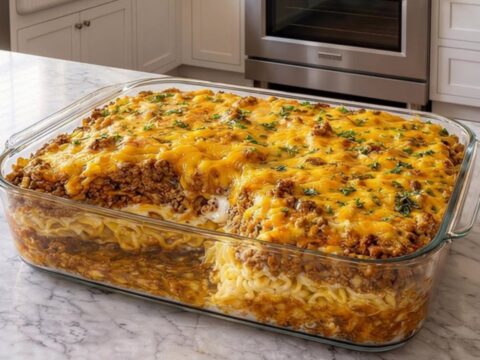 A golden, bubbly cheesy beef noodle casserole in a glass dish on a marble countertop.