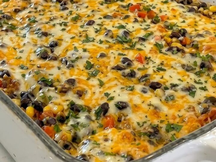 A whole white casserole dish filled with baked taco lasagna topped with bubbling cheddar, black beans, corn