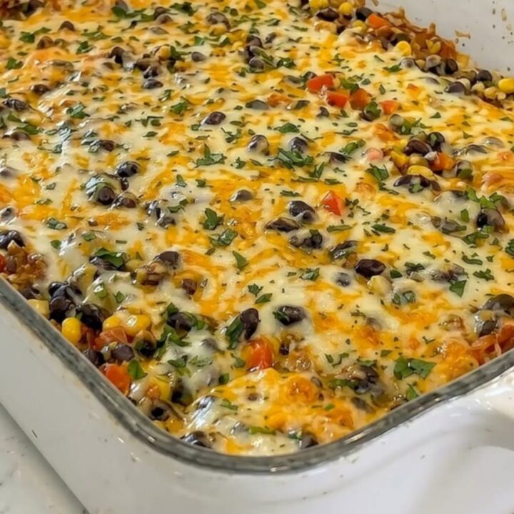 A whole white casserole dish filled with baked taco lasagna topped with bubbling cheddar, black beans, corn