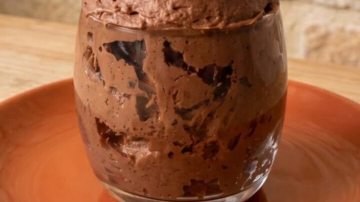 A silver spoon scooping into a rich, airy portion of two-ingredient chocolate mousse in a clear glass.
