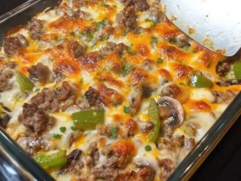 A steaming, cheesy Philly cheesesteak casserole in a glass dish with a golden melted cheddar topping.