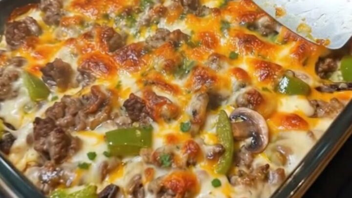 A steaming, cheesy Philly cheesesteak casserole in a glass dish with a golden melted cheddar topping.