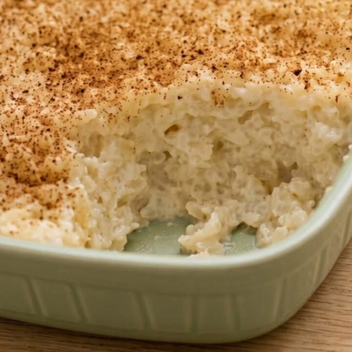 A close-up of a spoon scooping into a creamy, cinnamon-dusted sugar-free rice pudding in a green dish.