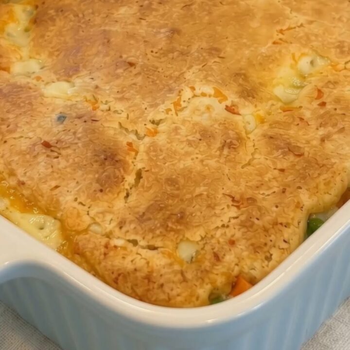 A golden-brown baked chicken cobbler in a white ceramic casserole dish glistening under warm kitchen lights.