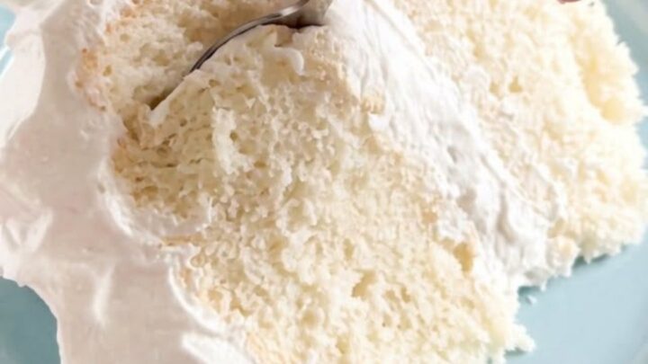 A pristine slice of fluffy sugar-free white cake with billowy white frosting on a blue plate
