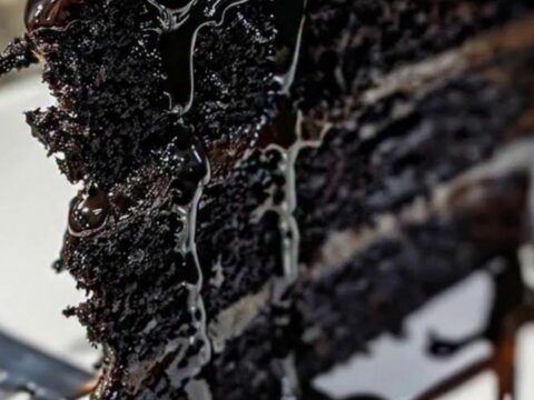 A towering three-layer chocolate cake with a glossy, decadent dark chocolate ganache dripping down the sides.