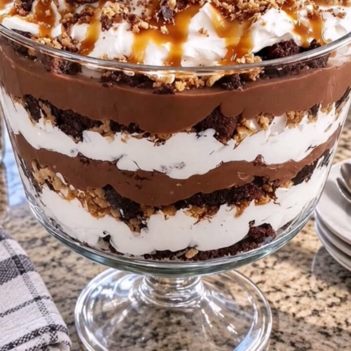 A clear glass bowl filled with layers of brownies, chocolate pudding, and whipped cream