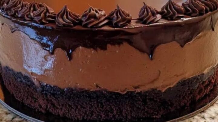 Gâteau mousse au chocolat brillant avec rosettes sur un comptoir en granit.