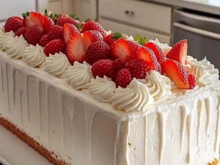 Gâteau rectangulaire aux fraises décoré de chantilly, présenté sur un plateau blanc dans une cuisine lumineuse.