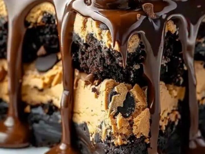 Glossy chocolate ganache dripping down a tiered cookie dough brownie cake on a white plate.