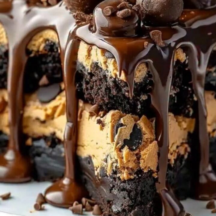 Glossy chocolate ganache dripping down a tiered cookie dough brownie cake on a white plate.