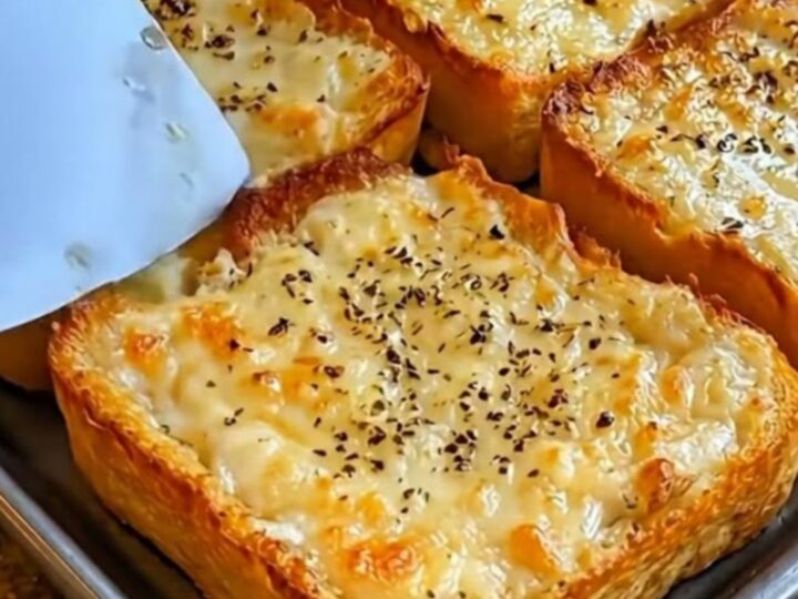 A sheet pan filled with six slices of golden-brown garlic cheese bread topped with fresh parsley.