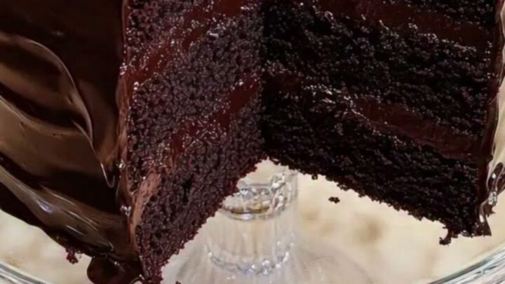 Gâteau au chocolat à trois étages sur un présentoir en verre avec une part découpée.