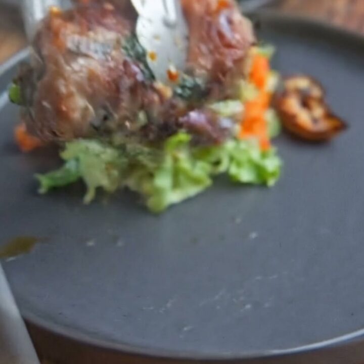 A close-up of a perfectly seared beef roll sliced to reveal vibrant spinach inside on a dark plate.