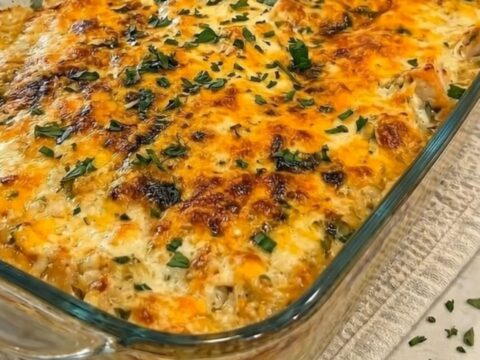 A steaming portion of cheesy chicken broccoli and rice casserole being scooped from a glass dish with a dramatic cheese pull.
