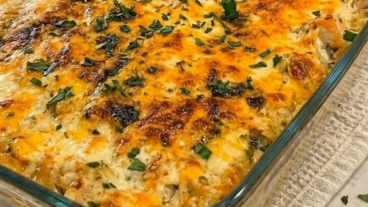 A steaming portion of cheesy chicken broccoli and rice casserole being scooped from a glass dish with a dramatic cheese pull.