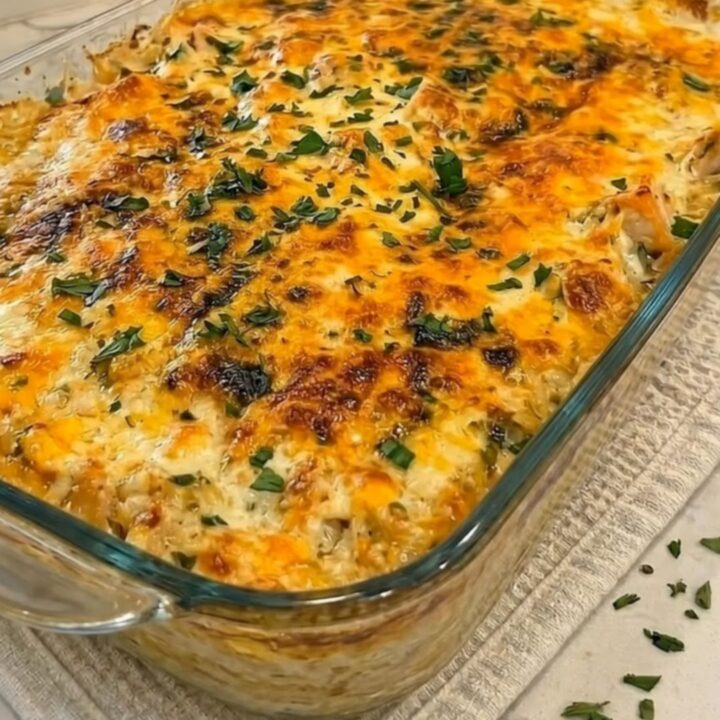 A steaming portion of cheesy chicken broccoli and rice casserole being scooped from a glass dish with a dramatic cheese pull.