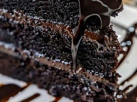 Une part de gâteau au chocolat noir nappée de ganache brillante sur une assiette blanche.