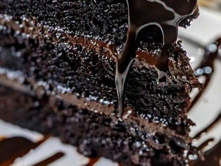 Une part de gâteau au chocolat noir nappée de ganache brillante sur une assiette blanche.