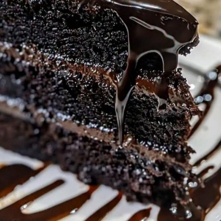 Une part de gâteau au chocolat noir nappée de ganache brillante sur une assiette blanche.