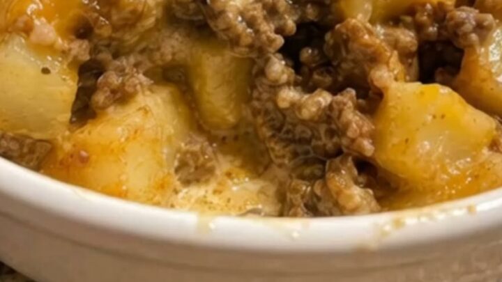A steaming white bowl filled with creamy taco seasoned ground beef, tender diced potatoes, and melted cheddar cheese