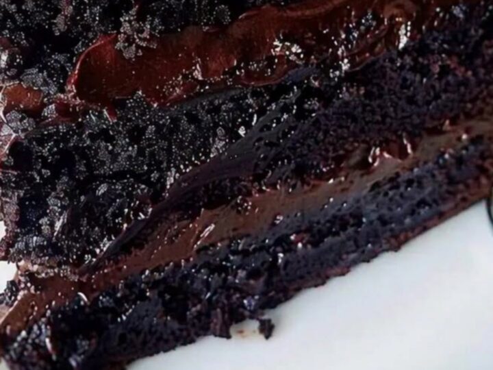 Une part de gâteau au chocolat brillant avec une ganache onctueuse sur une assiette blanche.